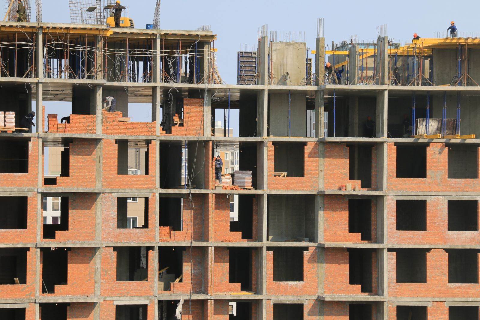 Construction workers working on a high-rise building frame with brickwork and scaffolding